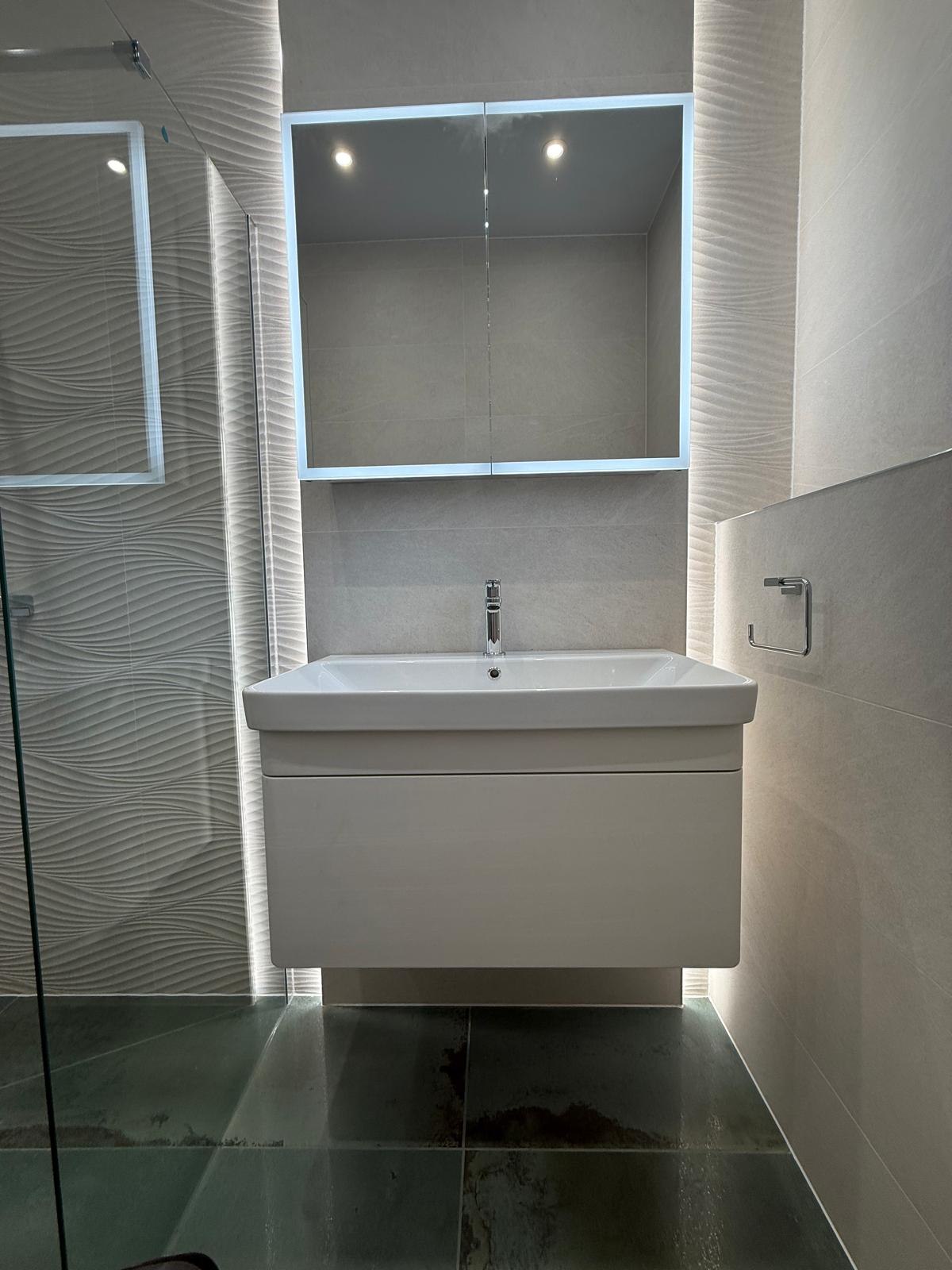 Floating white vanity beneath illuminated storage niches with textured wave tiling