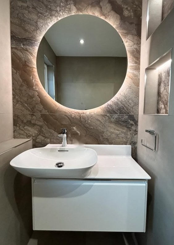 Round backlit mirror mounted on marble feature wall above white basin